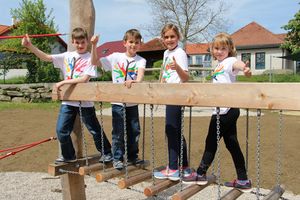 Vier Kinder balancieren auf einer Holz-Hängebrücke.