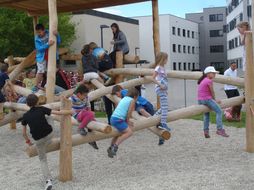 Kinder klettern auf einer Spielmöglichkeit aus vielen Holz-Stämmen herum.