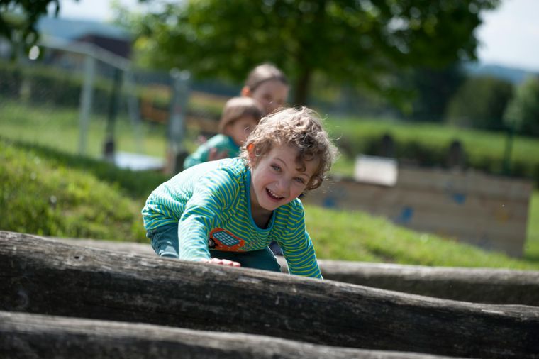 Bub klettert über Baumstamm am Spielplatz