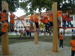 Kinder in orangen T-Shirts klettern auf einem Kletter-Parcours aus Holz