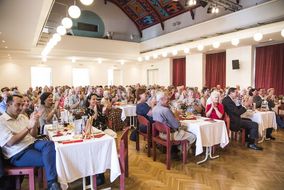 Ein dekorierter Saal ist voll mit begeisterten Zuhörerinnen und Zuhörer.