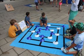 Fünf Buben sitzen am Boden und spielen Mühle in Lebensgröße