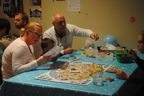 Familie sitzt an Tisch und spielt Gesellschaftsspiel.