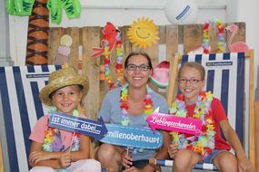 Zwei Mädchen und eine Dame lachen auf Sonnenstühlen sitzend in die Kamera