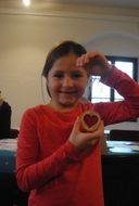 Mädchen zeigt ihren selbst gebastelten Schmuck in die Kamera.