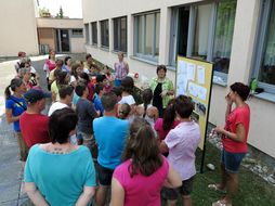 Eine Gruppe Erwachsener und Kinder schaut gespannt auf eine Tafel, an welcher die Gestaltungsskizze des neuen Schulfreiraumes angebracht ist