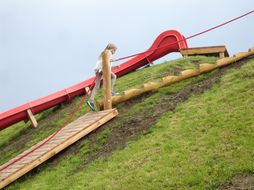 Ein Mädchen geht die Stiegen zu einer roten Rutsche auf einem Spielplatz hinauf.