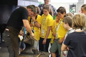 Kinder in gelben T-Shirts sehen gespannt einem Betreuer zu 