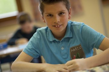 Bub lächelt bei der Kinderbetreuung im Rahmen der schulischen Tagesbetreuung in die Kamera