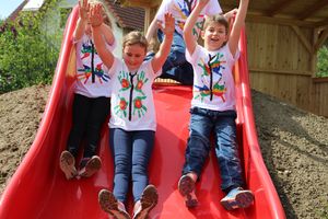 Drei Kinder rutschen am Schulfreiraum in Maria Laach eine rote Rutsche hinunter.