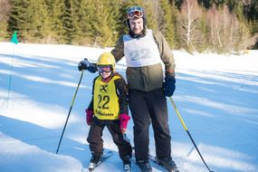 Mann und Kind lachen bei strahlendem Sonnenschein auf der Piste in die Kamera