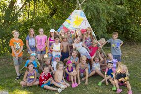 Eine Gruppe Kinder sitzt vor einem bunt bemalten Tipi