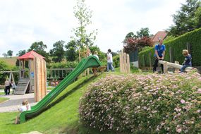 Spielplatz mit einer grünen Rutsche und vielen schönen Blumen.