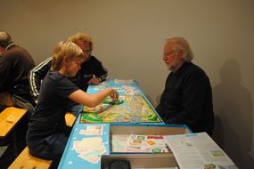 Mehrere Personen sitzen am Tisch und spielen ein Brettspiel.