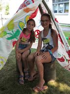 Zwei Mädchen sitzen in einem bunt bemalten Tipi und lachen in die Kamera