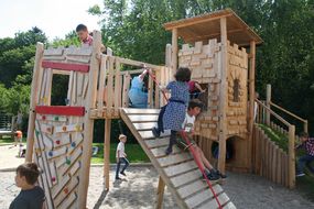 Kinder klettern bei der Eröffnung des Spielplatz auf einer hölzernen Kletterburg