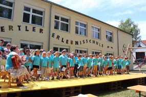 Kinder in blauen T-Shirts singen bei der Eröffnung des Schulfreiraums.