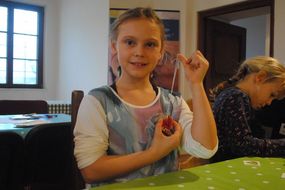 Mädchen zeigt ihre selbst gebastelte Kette in die Kamera.