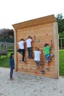 Kinder klettern auf einer hölzernen Kletterwand.