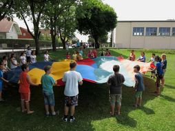 Eine Gruppe aus Kindern und Erwachsenen hält ein großes, buntes Schwungtuch in Händen.