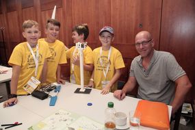 Vier Kinder in gelben T-Shirts und ein Mann lachen bei der 3. Kinder Business Week in die Kamera