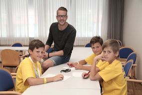 Drei Buben und ein Betreuer sitzen um den Tisch und lachen in die Kamera.