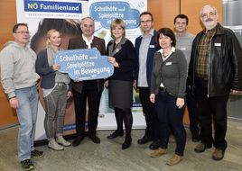 Landesrätin Schwarz hält zusammen mit einer Frau und einem Mann beim Seminar "Schul(t)räume" ein Schild mit der Aufschrift "Schulhöfe und Spielplätze in Bewegung" in die Kamera.
