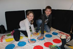 Mädchen und Bub spielen zusammen Twister.